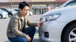 車のバンパーについた擦り傷を不安そうな表情で確認する日本人男性