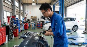 整備工場のピット内で車のバンパーを丁寧に研磨・補修作業するプロの日本人整備士