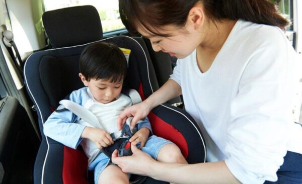 明るい車内で日本人の母親が子どものチャイルドシートのベルトを整える様子。5人乗り車の後席の広さと子どもの乗せ降ろしを確認する場面。