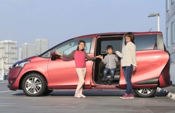 白いスライドドア車と淡いグリーンのコンパクトミニバンのそばで、子どもと一緒に乗り降りする日本人家族。5人乗りスライドドア車の送迎シーン。